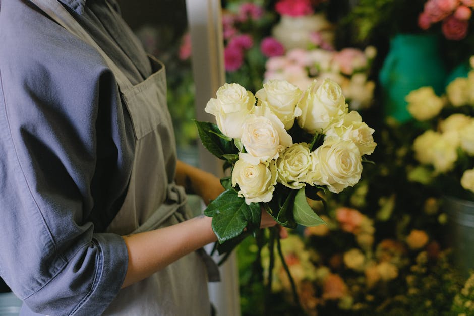 Florist holding a bouquet of white roses in a flower shop, showcasing vibrant floral arrangements.